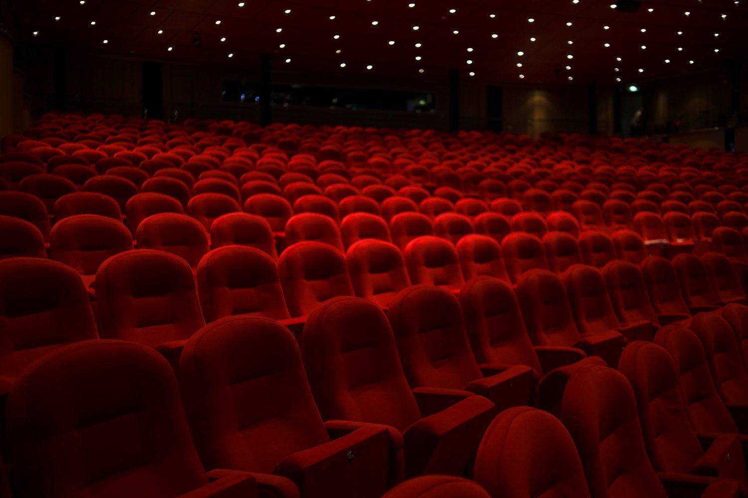 Widownia teatru z czerwonymi fotelami i kurtyną w ciepłym świetle